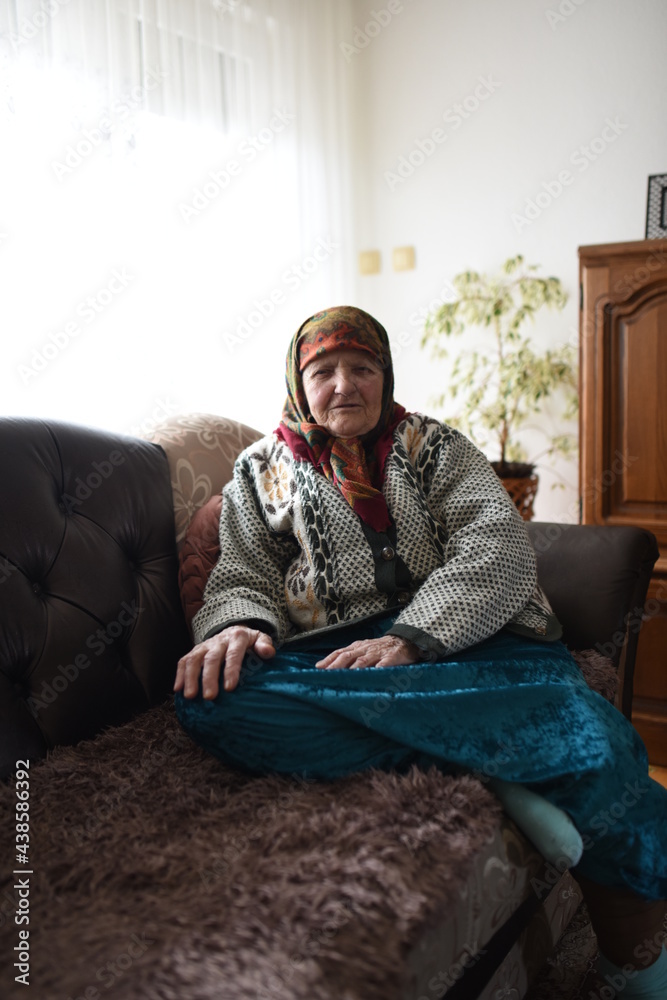 a very old woman in traditional Muslim clothes sitting in the house next to the window