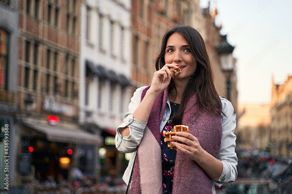Happy girl walk and eat Belgian waffles on city street