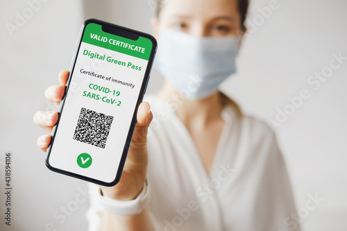 Young caucasian woman in mask holding smartphone with digital green pass and QR code on the screen. Health passport or certificate of immunity. Traveling without restrictions. Vaccinated person
