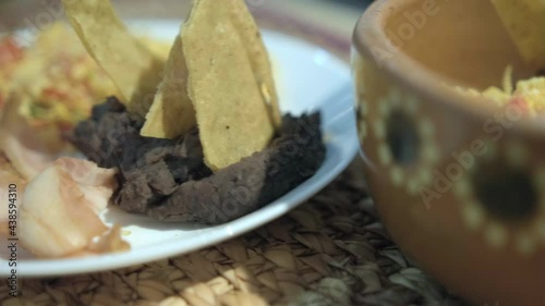 Mexican-style eggs, bacon, and refried beans with tortilla chips on white plate