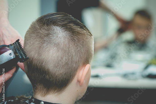 Professional barber doing haircut for kid. Hairdress for children. side view portrait barbershop.Back view.Toned