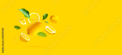 Juicy ripe flying yellow lemons, green leaves on yellow background. Creative food concept. Tropical organic fruit, citrus, vitamin C. Lemon slices. Summer minimalistic bright fruit background. Banner