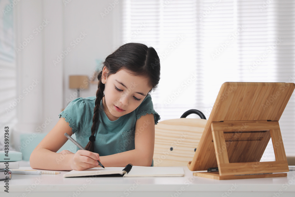 Little girl doing homework with tablet at table in room Little girl doing homework with tablet at table in room