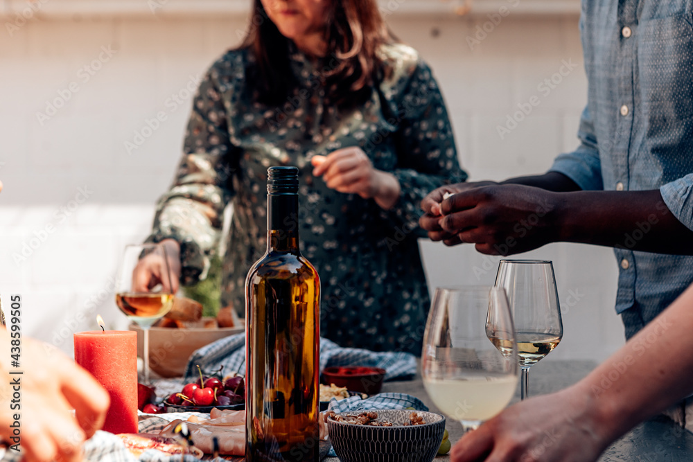 bottle of wine on the party table with appetizers and tapas. Accidental people around a buffet with ready to eat food.