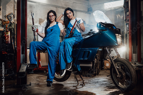 Two female mechanic posing next to a sportbike in authentic workshop garage