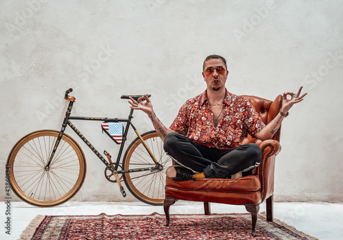 Fotografía Tattooed stylish gangster sits on a armchair in a lotus pose, looks very express
