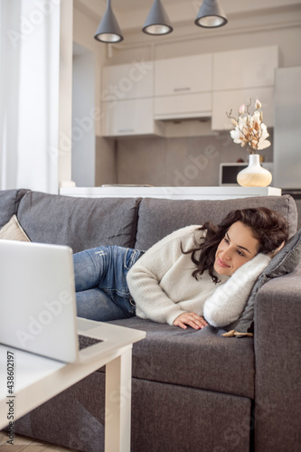 A woman in white sweater lying on the sofa and watching something online