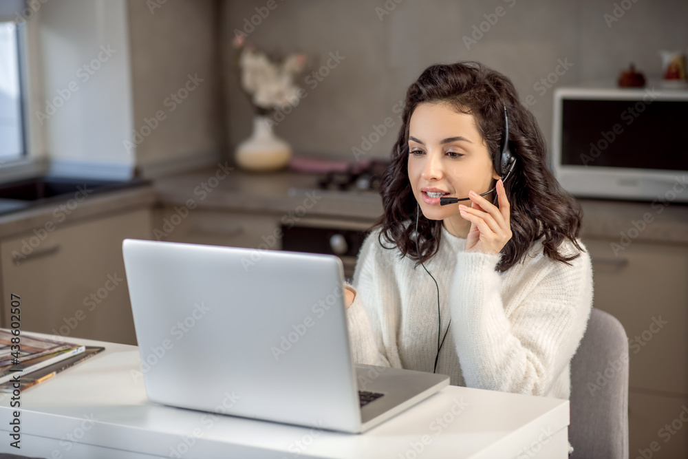 An operator in earphones sitting at the laptop while working from home An operator in earphones sitting at the laptop while working from home