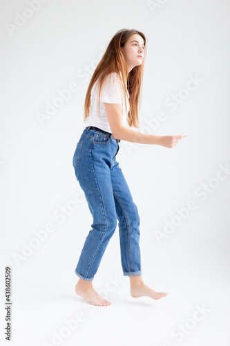 young attractive caucasian woman with long hair in t-shirt and blue jeans dances on white studio background. skinny pretty female dancing on cyclorama with bare feet. model tests of beautiful lady