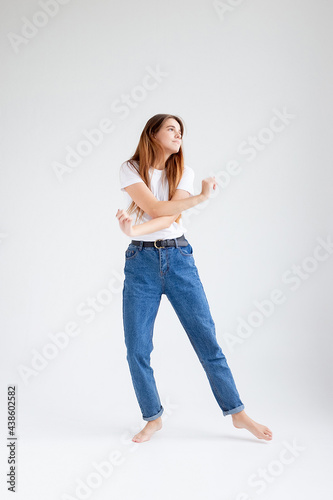 young attractive caucasian woman with long hair in t-shirt and blue jeans dances on white studio background. skinny pretty female dancing on cyclorama with bare feet. model tests of beautiful lady