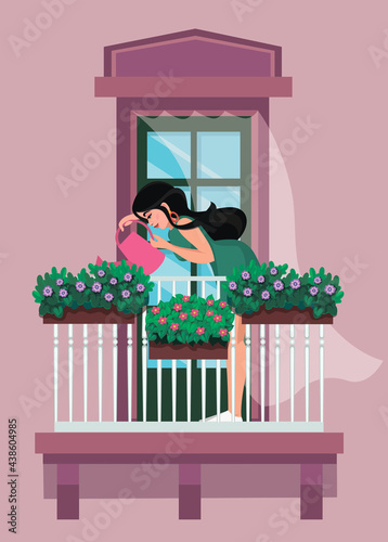 The girl is watering the plants. A girl with long hair stands near the window with a watering pad and watering the plants in a flowerpot on the balcony