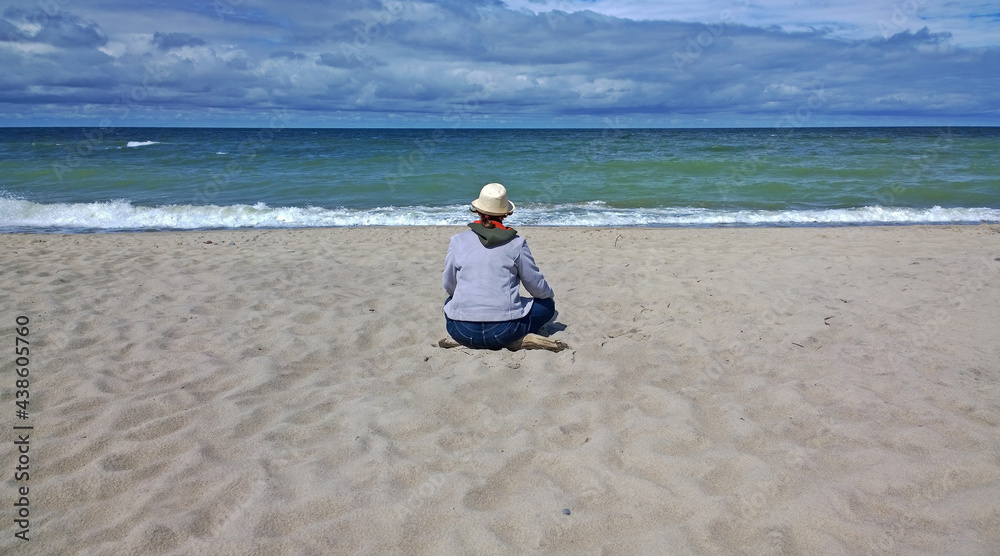 Rear view of woman sitting on the beach and looking at the sea