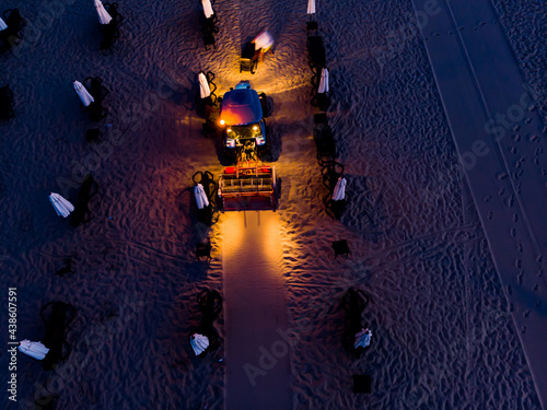 The aerial shot of sand cleaner. Beach cleaning machine. Tractor with lights on raking sand in the dark after when the tourists have left the beach. Bulgaria, Slanchev Bryag