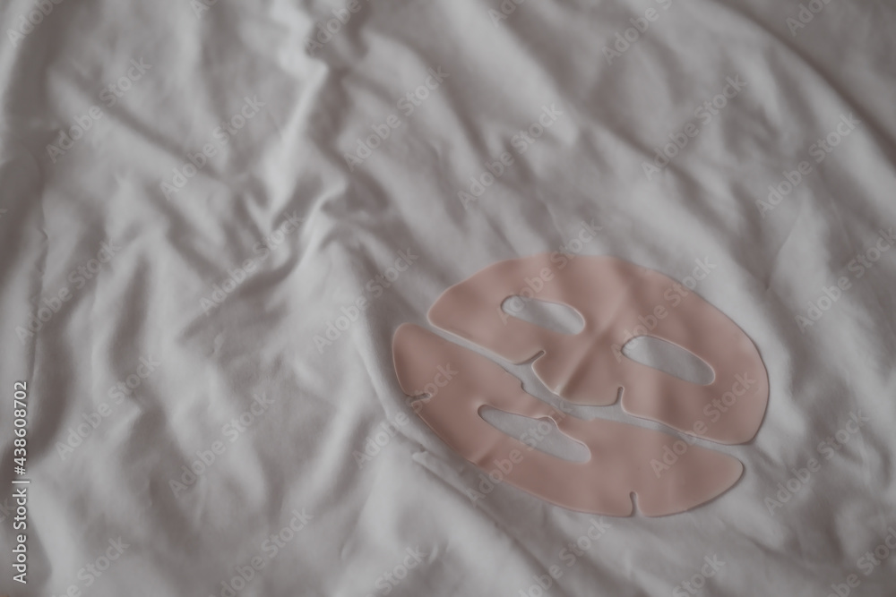Light pink gel facial sheet mask on white bed sheets background. Copyspace for text, minimalist beauty product, blogging concept, stylish pastel colored, fade Light pink gel facial sheet mask on white bed sheets background. Copyspace for text, minimalist beauty product, blogging concept, stylish pastel colored, fade