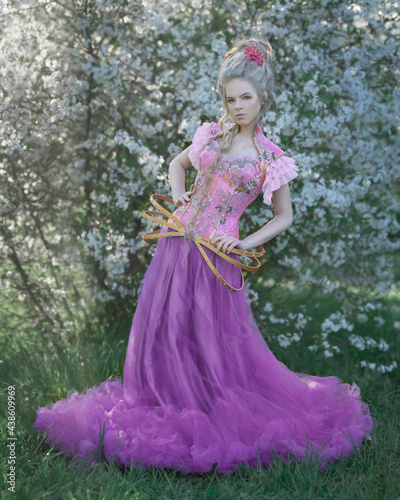 Blond girl in a pink corset in a blooming apple orchard