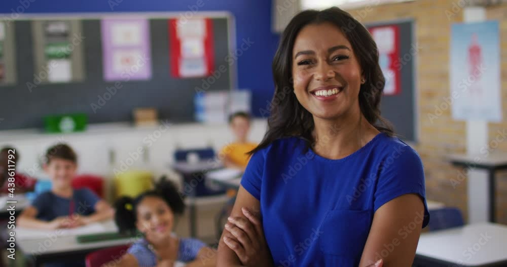 Portrait of happy mixed race female teacher standing in classroom with children in background