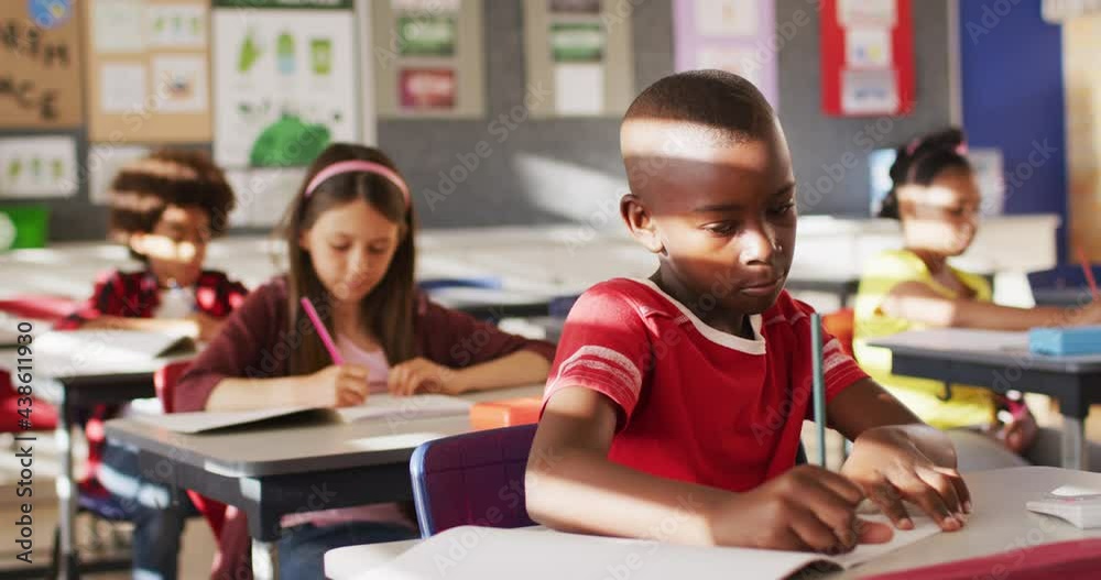 Portrait of african american schoolboy sitting in class, making notes, looking at camera Portrait of african american schoolboy sitting in class, making notes, looking at camera