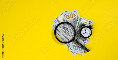 paper american hundred dollar bills and a magnifying glass on a yellow background. The concept of search for earnings, profit with less time