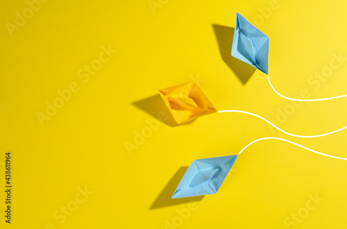paper boats sail in different directions on a yellow background. the concept of leadership, achieving goals and disunity photo