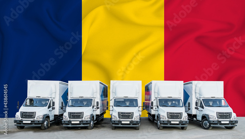 Romania flag in the background. Five new white trucks are parked in the parking lot. Truck, transport, freight transport. Freight and logistics concept