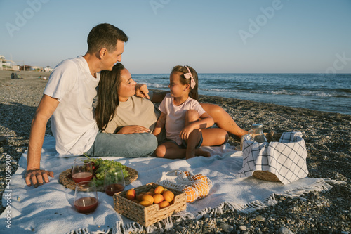 Family spending time together outdoor. Picnic lunch with fruits by the seaside. Happy people eating healthy food and sitting on blanket on the beach. Summer leisure concept.