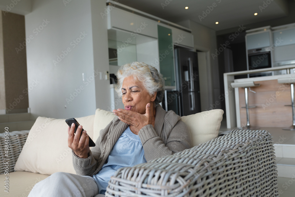 Mixed race senior woman sitting on sofa making video call using smartphone Mixed race senior woman sitting on sofa making video call using smartphone