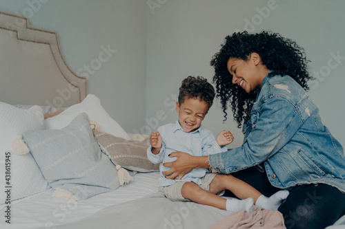 Loving afro american mother tickling son while having fun together in bedroom