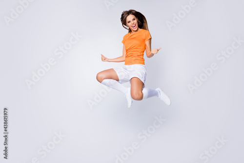 Full length photo of excited lady player soccer jump raise fists celebrate league competition win wear orange uniform t-shirt shorts cleats long knee socks isolated white color background