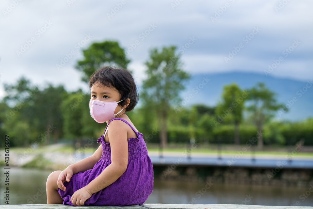 Adorable Little girl wearing protective face mask sitting at lake outdoor.