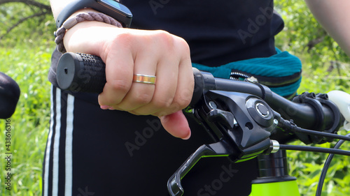 Woman's hand with ring on the handlebars of a mountain bike in the park close-up. The biker leans on the handlebars of the bike.