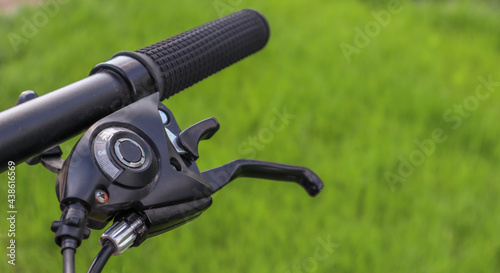 Mountain bike steering wheel on green grass background. Details of sporting events. Close up black mountain bike knob and derailleur knob, left shifter.