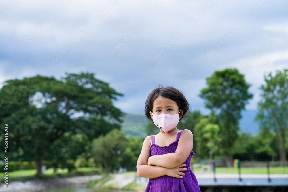 Adorable little girl stand with arms crossed at park wearing protective face mask Adorable little girl stand with arms crossed at park wearing protective face mask