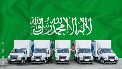 Saudi Arabia flag in the background. Five new white trucks are parked in the parking lot. Truck, transport, freight transport. Freight and logistics concept