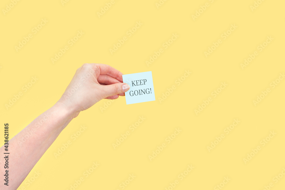 The hand holds a sticky note with inscription Keep going The hand holds a sticky note with inscription Keep going