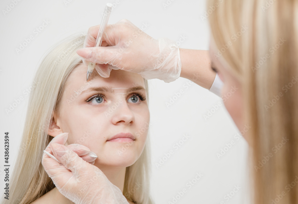 Cosmetologist measures the proportions of the eyebrows with the ruler before permanent make-up for eyebrows