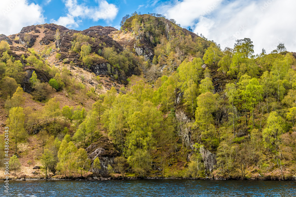 A view of the wooded and rocky southern shore of Loch Katrine in the Scottish Highlands on a summers day A view of the wooded and rocky southern shore of Loch Katrine in the Scottish Highlands on a summers day