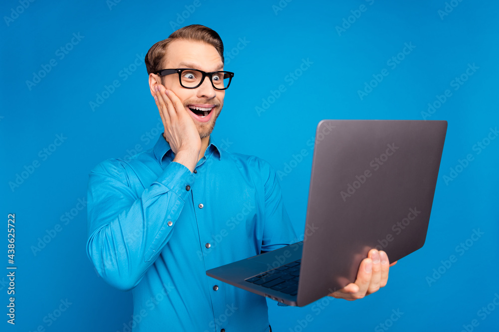 Profile side photo of young business man amazed shocked surprised look laptop news isolated over blue color background Profile side photo of young business man amazed shocked surprised look laptop news isolated over blue color background
