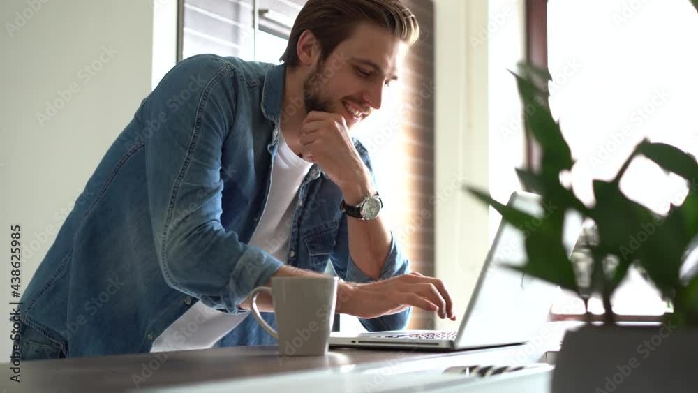 Smiling man with glasses works from home in his kitchen using a laptop. Remote work and remote learning