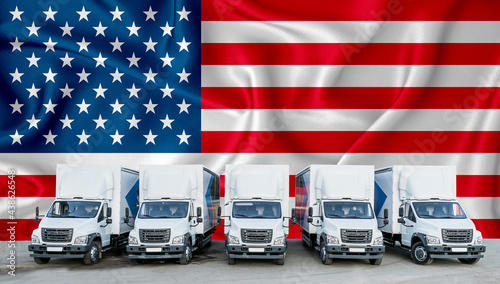 US flag in the background. Five new white trucks are parked in the parking lot. Truck, transport, freight transport. Freight and logistics concept
