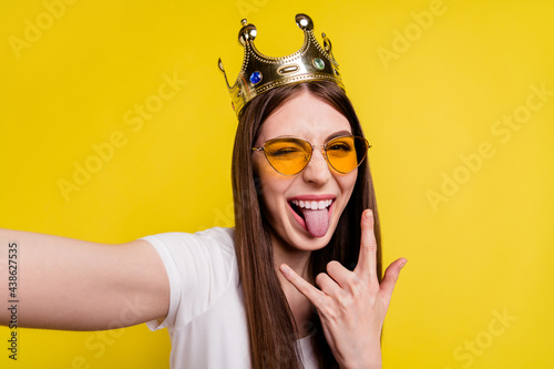 Photo of young excited girl happy positive smile wink eye show rock sign wear crown isolated over yellow color background