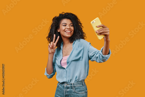 Beautiful young African woman in casual clothing taking selfie and smiling