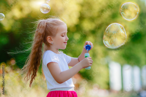 little girl blows soap bubbles in the park in summer