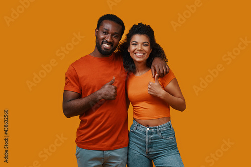 Beautiful young African couple gesturing and smiling while standing against yellow background