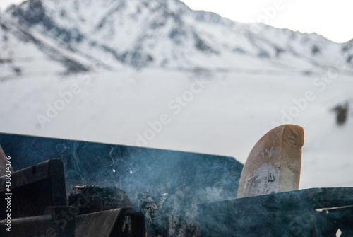 Trozo de queso sobre parrilla con montaña nevada de fondo - Temporada de Sky en Las Leñas