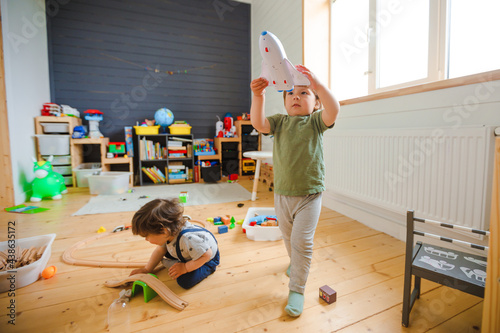 Little boys play with a wooden railroad in a stylish nursery.