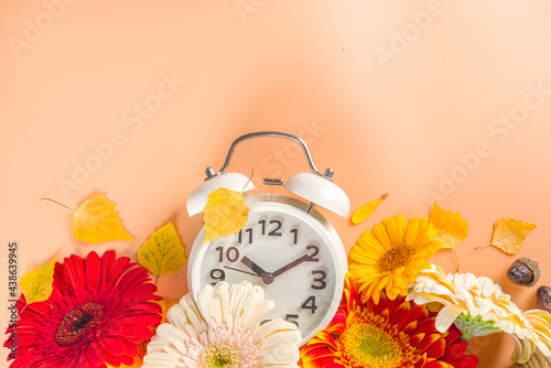 Fall Back Time. Daylight Savings End. Return To Winter Time. Autumn time change concept with Alarm Clock, with pumpkins, gerbera flowers, fall leaves, autumn decor flatlay top view copy space