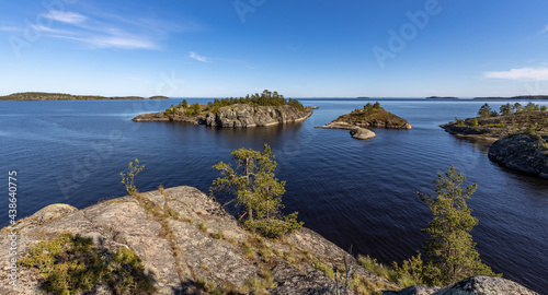 Summer landscape with rocks by the lake and pines. Lake landscape banner. The blue sky is reflected in the water.