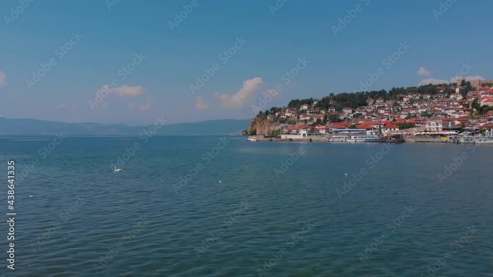 A huge lake of Ohrid, North Macedonia. Historic Medieval houses with red roofs are on the shore of blue water. Birds are swimming on surface. Beautiful scenic took with aerial drone 4K 30fps. A huge lake of Ohrid, North Macedonia. Historic Medieval houses with red roofs are on the shore of blue water. Birds are swimming on surface. Beautiful scenic took with aerial drone 4K 30fps.