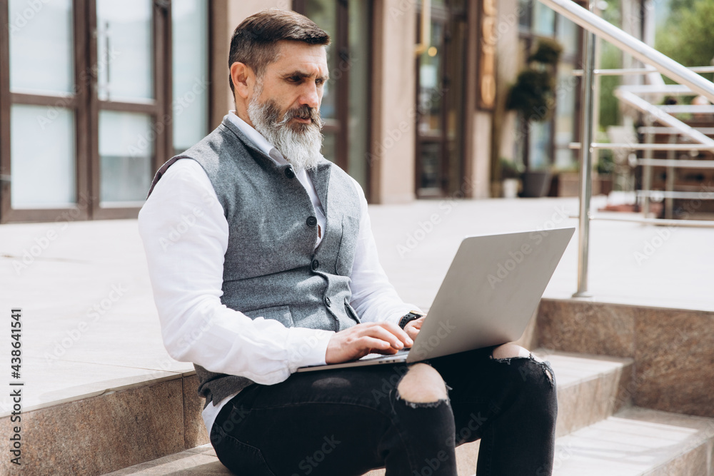 Senior man stylish man with gray beard spends time outdoors in laptop. Senior man stylish man with gray beard spends time outdoors in laptop.