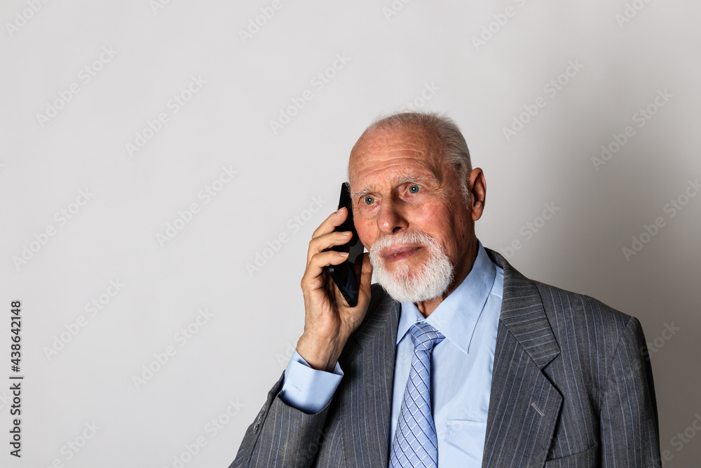Old man in blue is using a smart phone on gray background with copy space. Old man in blue is using a smart phone on gray background with copy space.